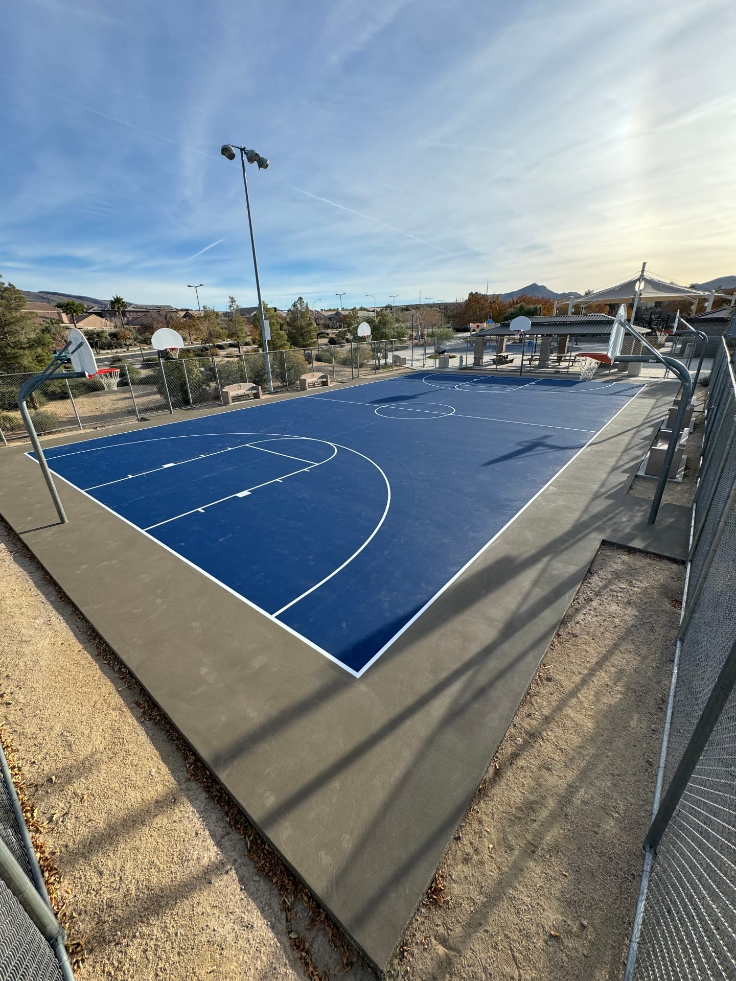 A freshly resurfaced blue basketball court in a community park in Las Vegas with white lines and chain-link fencing.
