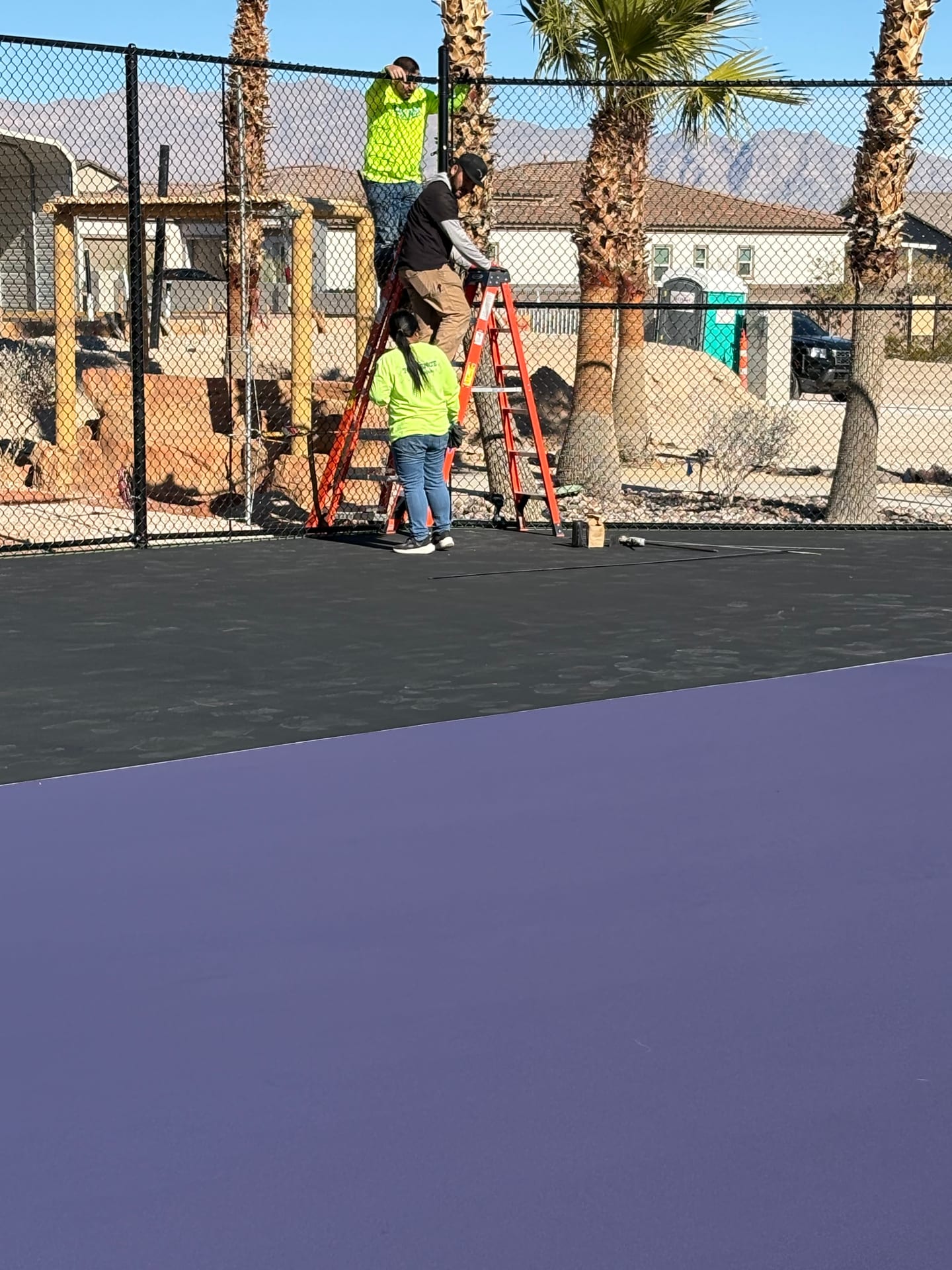 Professional crew installing black chain-link fencing around a purple and black athletic court in Las Vegas