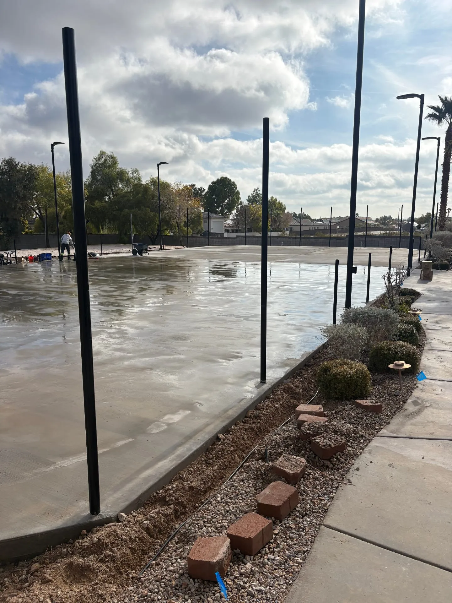 Freshly poured post-tension concrete court curing between 10 ft fence posts in Las Vegas, NV
