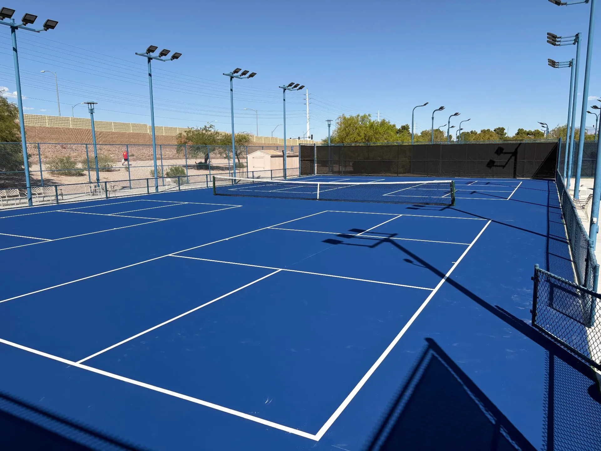Four newly resurfaced blue pickleball courts in Las Vegas with LED lighting and black perimeter fencing.