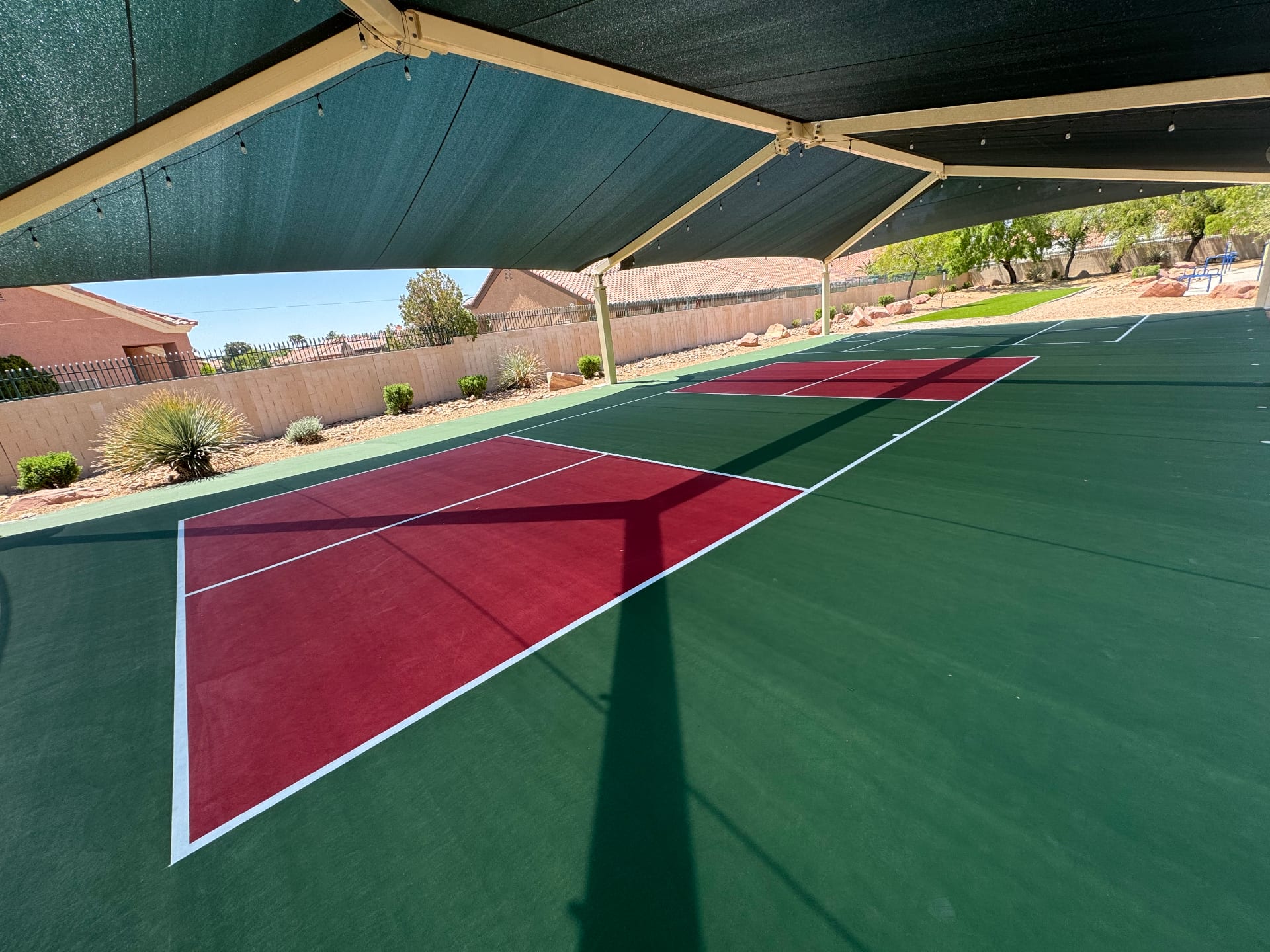 A newly resurfaced red and green backyard pickleball court in Las Vegas shaded by a large custom canopy structure.