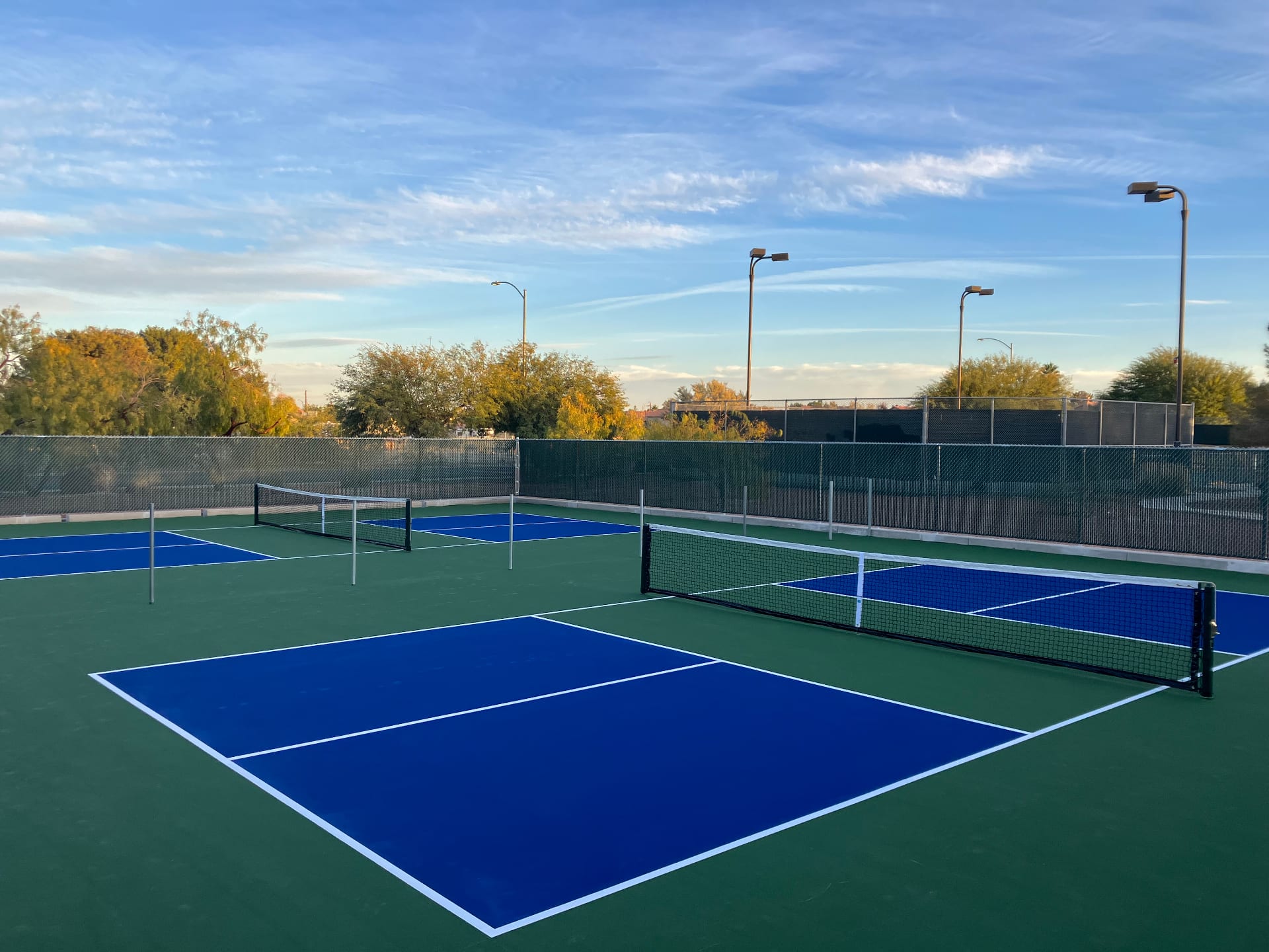 Newly resurfaced blue and green pickleball courts at Patriot Park in Las Vegas with chain-link fencing and court lighting.