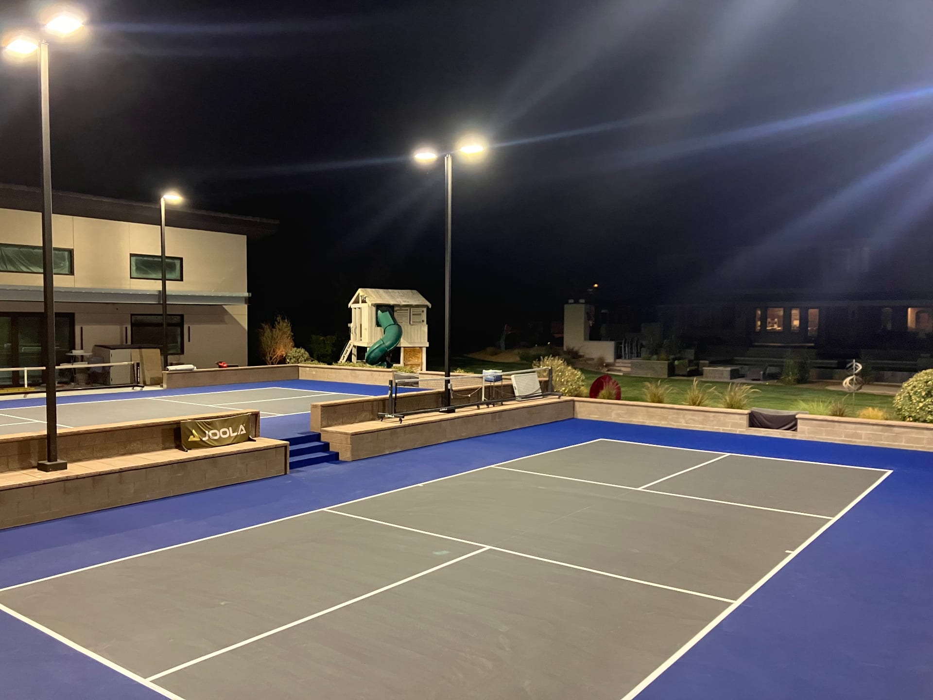 Night view of a residential backyard pickleball court in Las Vegas with LED lighting and blue and grey surfacing.