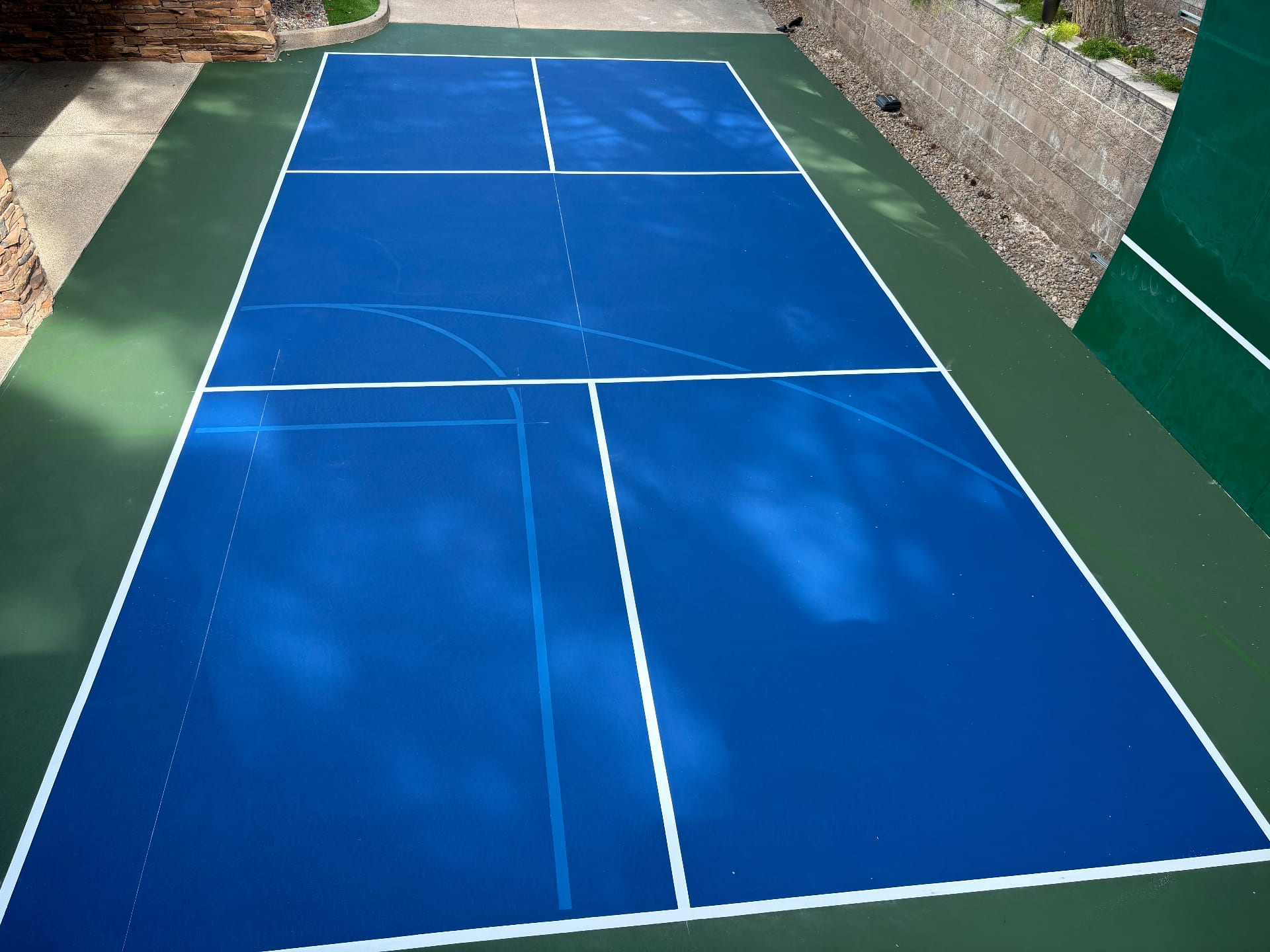A freshly resurfaced blue and green pickleball court in a residential backyard setting.