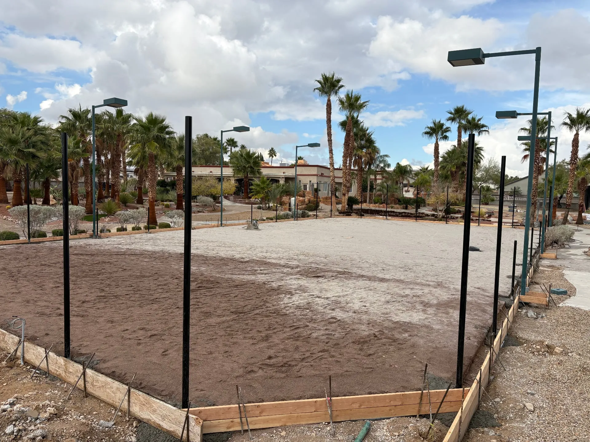Construction site of a tennis court in Las Vegas showing wooden formwork and vertical fence posts installed before concrete pouring.