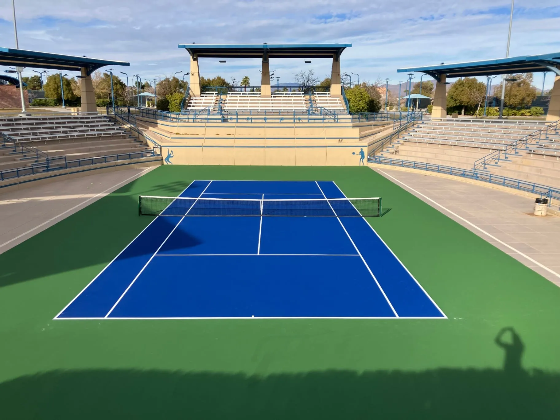 Professionally resurfaced blue and green tennis court at Darling Stadium in Las Vegas with tiered spectator seating.