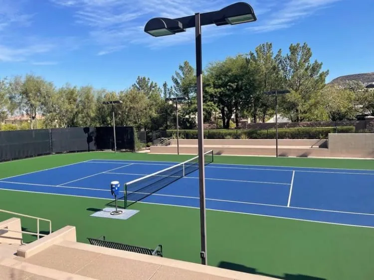 A professional tennis court with blue and green surfacing, stadium lighting, and black windscreen at Dragon Ridge in Henderson, NV.