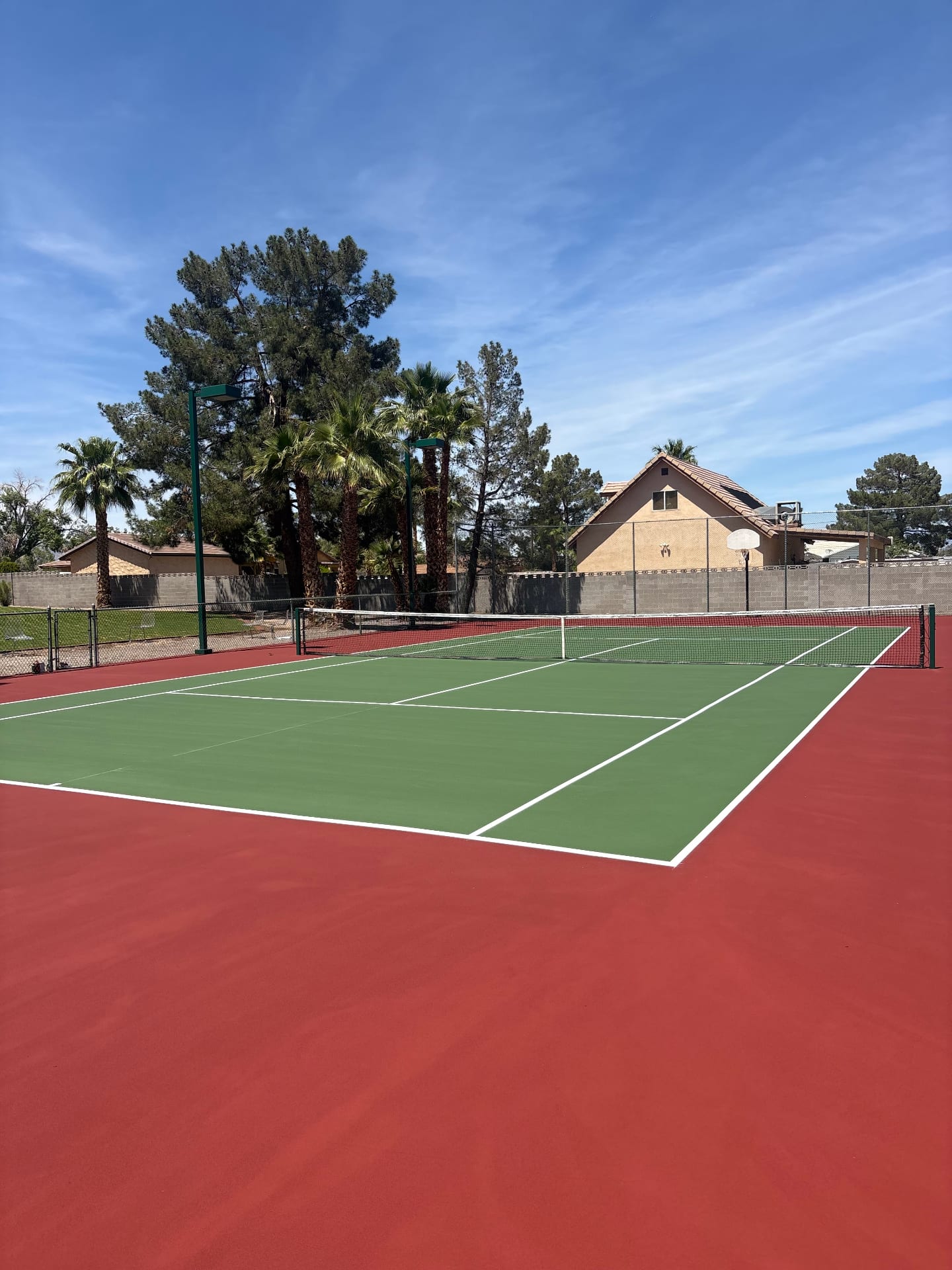 Newly resurfaced residential tennis court with red and green acrylic coating in Las Vegas backyard