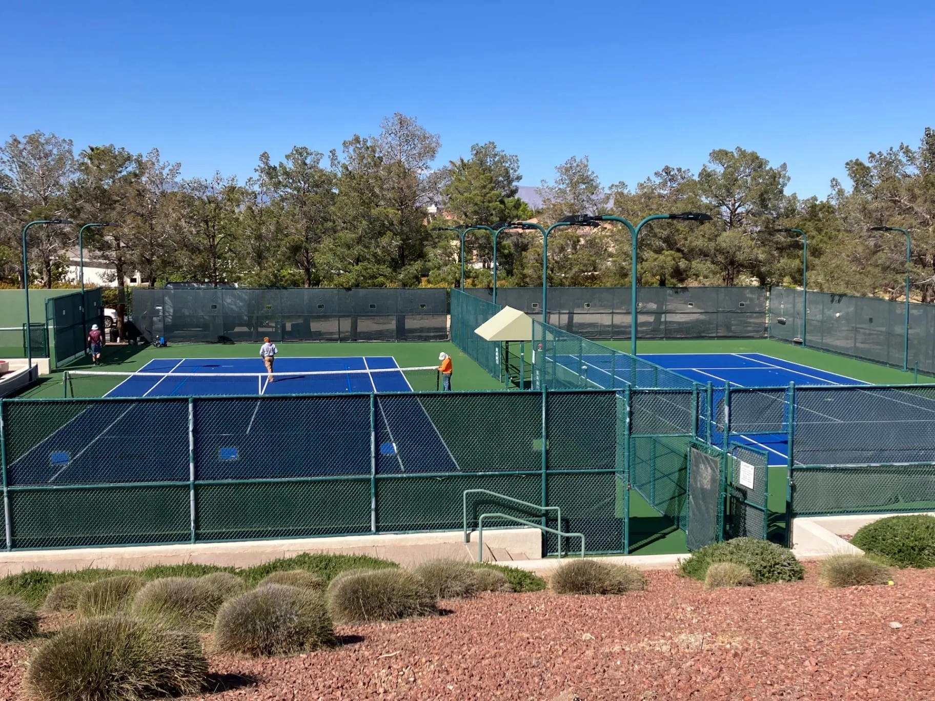 Two freshly resurfaced blue tennis courts at a Las Vegas club facility with green perimeter fencing and LED lighting.