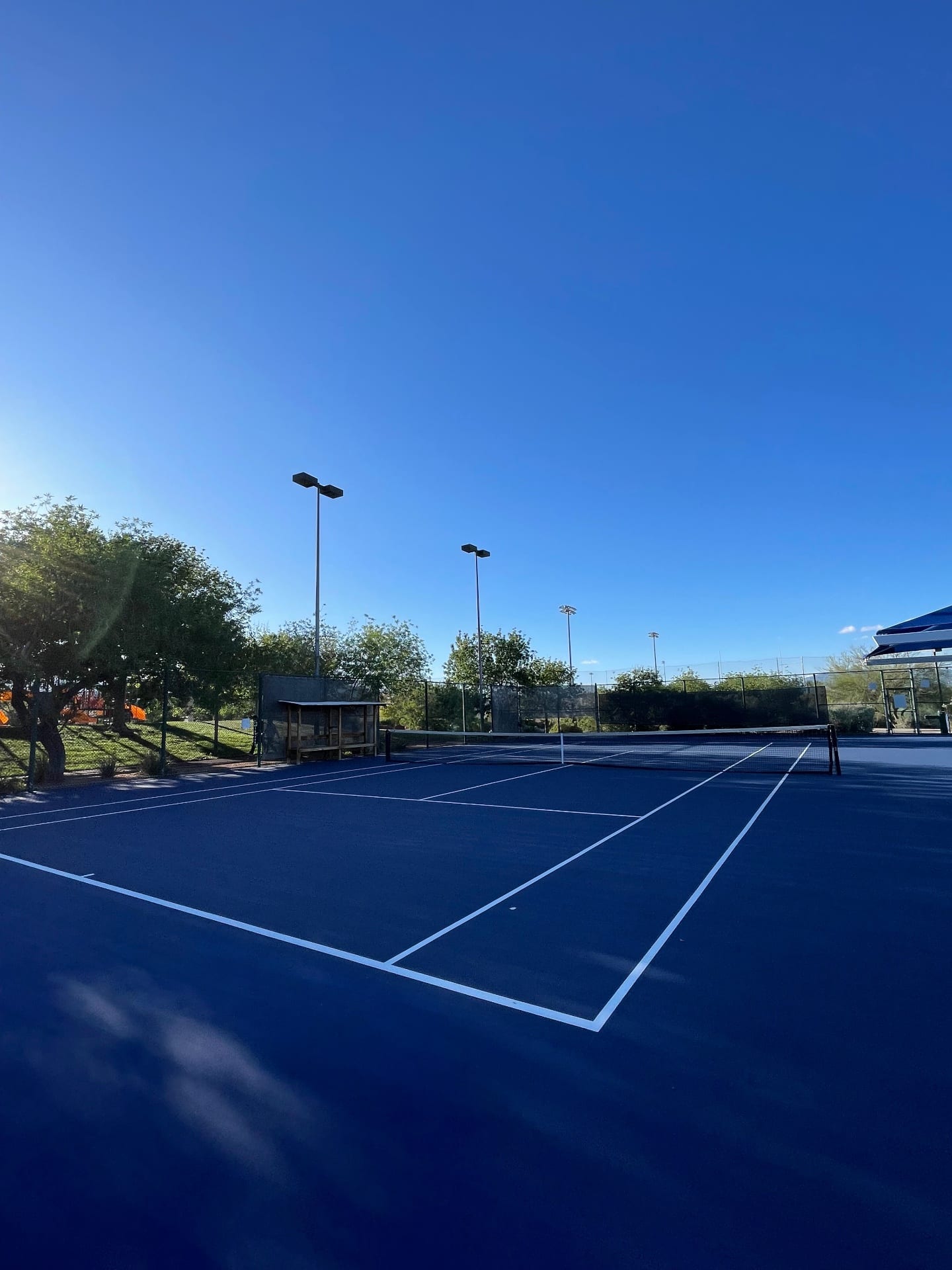 A freshly resurfaced all-blue tennis court in Las Vegas with white lines and stadium lighting.