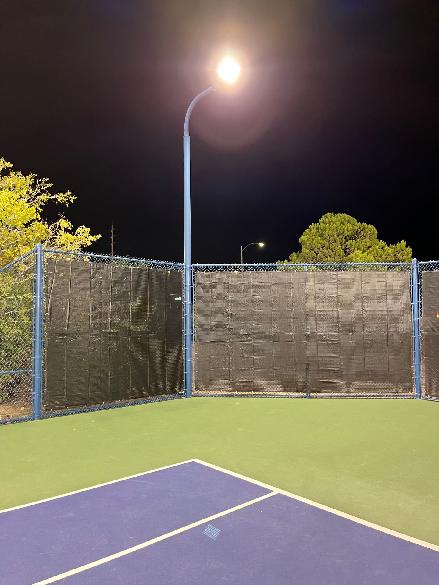 Black privacy windscreens installed on a blue chain-link fence at a night-lit athletic court in Las Vegas