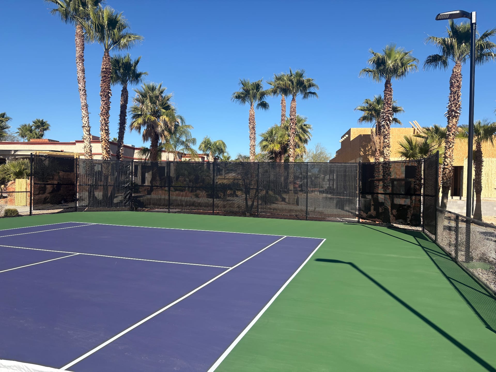 Black 9ft athletic court windscreens installed around a blue and green tennis court in Las Vegas