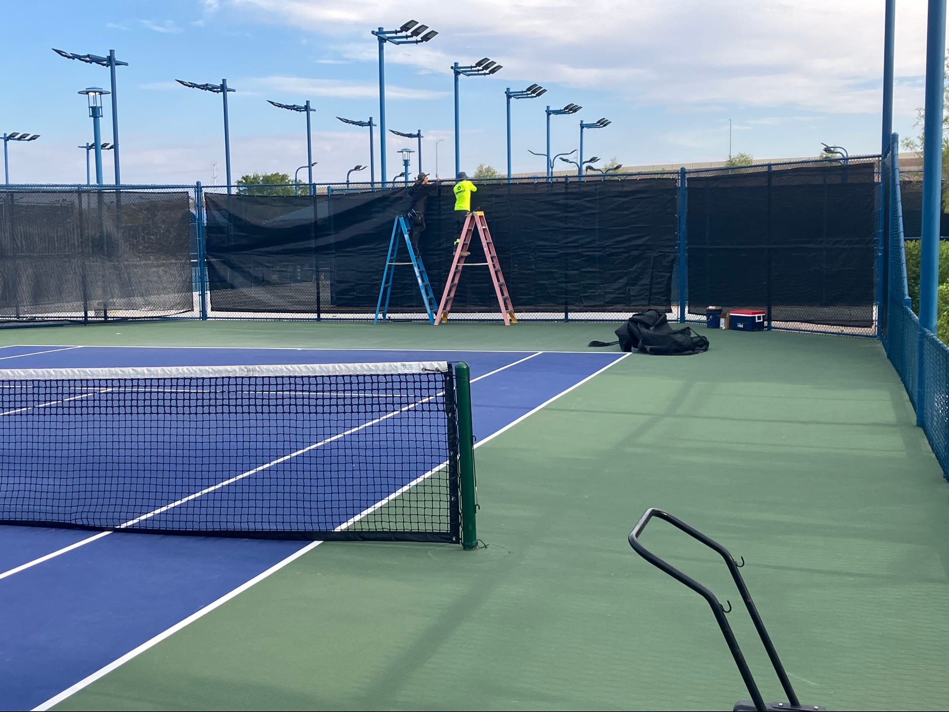 Technicians installing black windscreens on a tennis court fence in Las Vegas