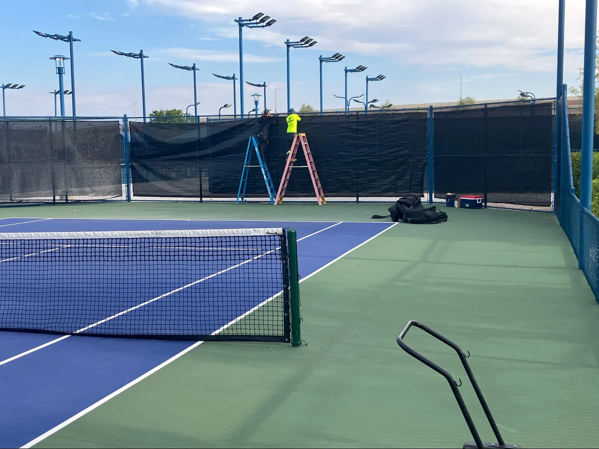 Crew hanging black windscreens on a tennis court fence in Las Vegas, NV